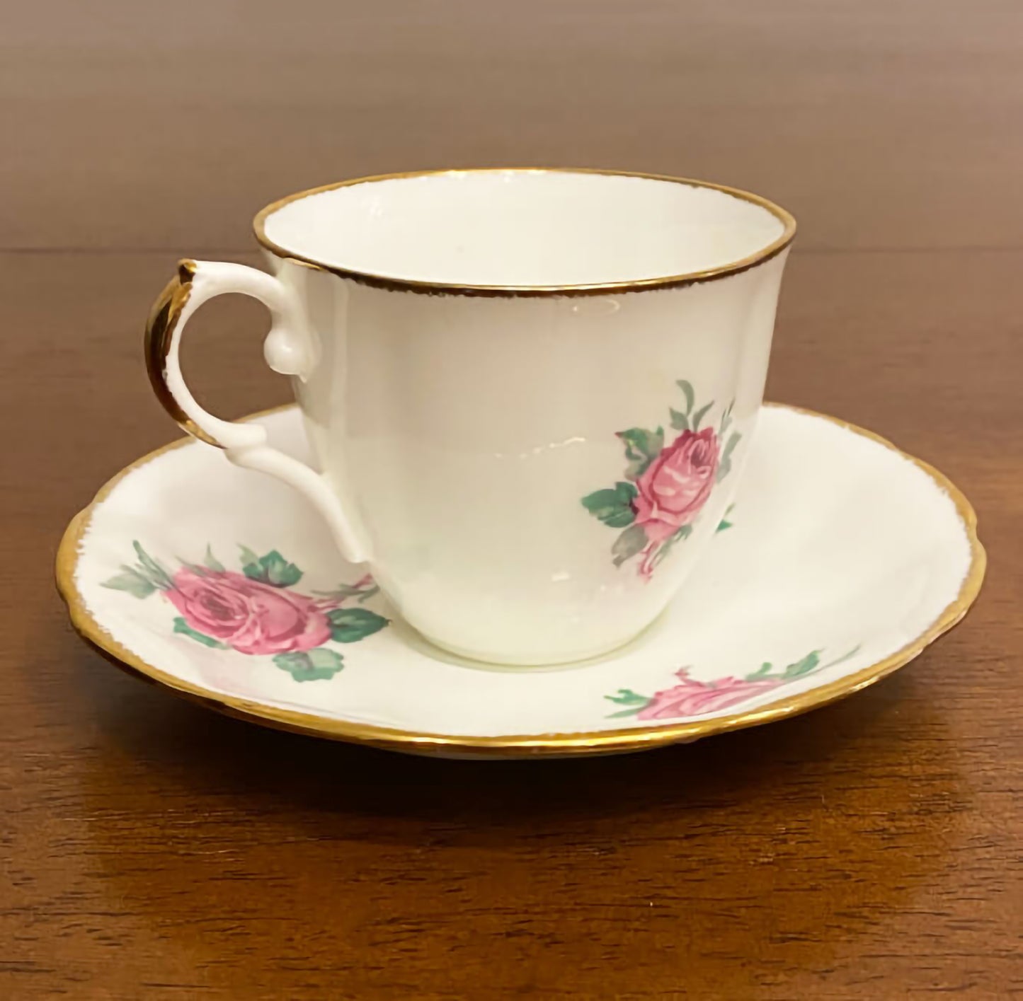 Jason-bone-china-collectible-teacup-and-saucer-set,-#J554,-featuring-pink-roses-and-green-leaves,-accented-by-gilt-trim-on-the-edge-of-the-cup-and-saucer.-Side-view.-Excellent-condition.-Makes-a-great-gift.-Shop-eBargainsAndDeals.com.